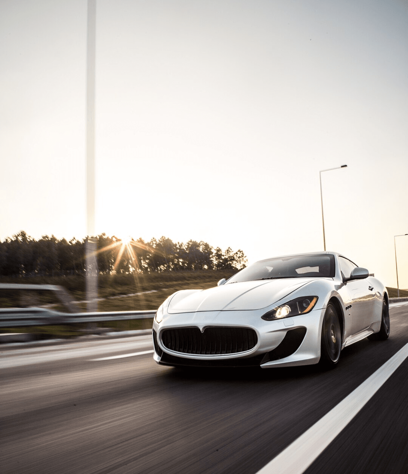 A Maserati GranTurismo driving on a highway at sunset